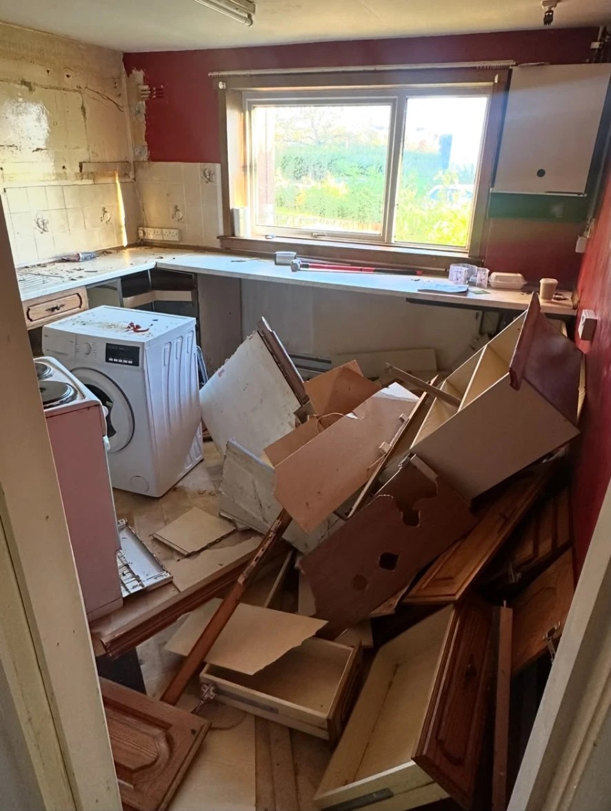 Kitchen mid strip-out with old units, doors and worktops stacked on the floor